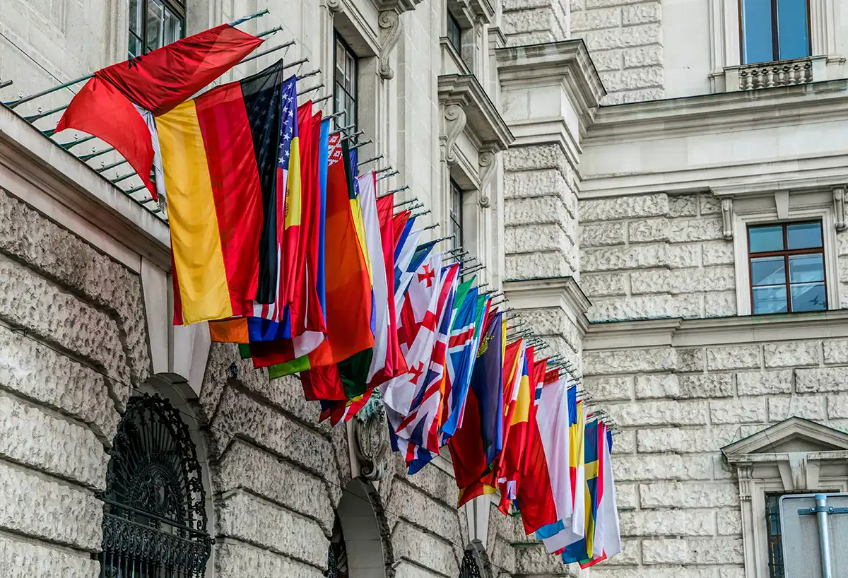 Row of national flags on the façade of a diplomatic building, symbolising the international missions a foreign service maintains around the world.